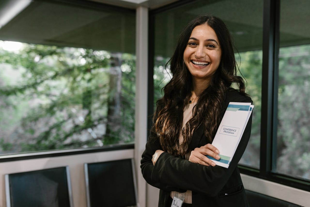 about-01 Confident woman holding conference program, smiling in modern indoor setting.